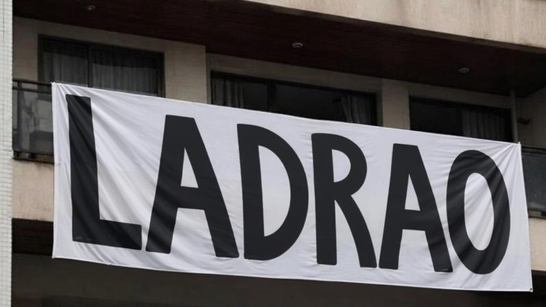 Na imagem, faixa com a palavra “ladrão” na janela do apartamento