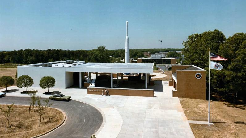 a low-slung brick and stucco building with a large rocket behind it