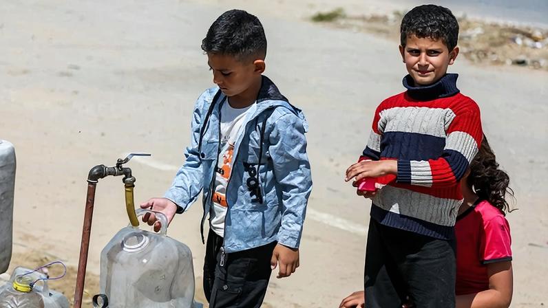 Crianças palestinas no campo de refugiados de Bureij enchem seus recipientes com água dos caminhões-pipa após ataques israelenses destruírem a infraestrutura na Cidade de Gaza. 28/04/2026