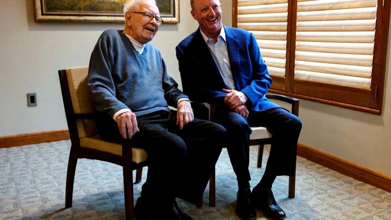 Warren Buffett e Greg Abel sorrindo em cadeiras.