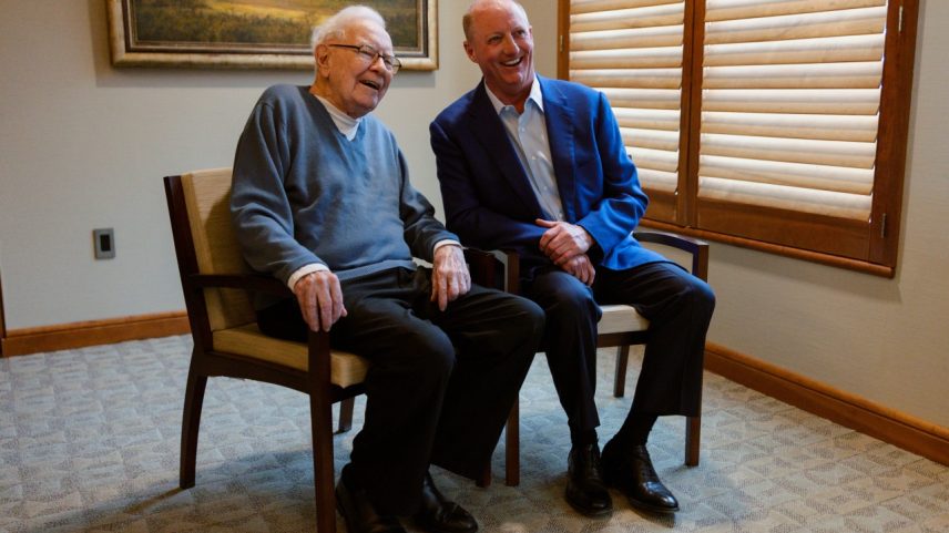 Warren Buffett e Greg Abel sorrindo em cadeiras.