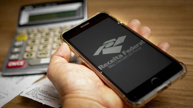 Imagem colorida de um celular com o símbolo da Receita Federal Imposto de Renda consulta - Metrópoles