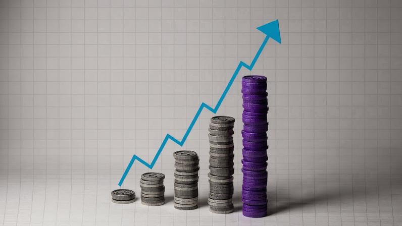 Pilhas de moedas em diferentes alturas sobre fundo quadriculado com linha azul em formato de gráfico ascendente.