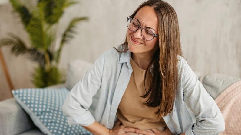 Foto colorida de mulher sentada e com a mão na barriga - Metrópoles