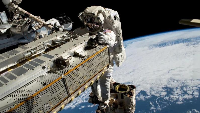 Astronaut Woody Hoburg rides the Canadarm2 robotic arm while maneuvering a roll-out solar array during a spacewalk.