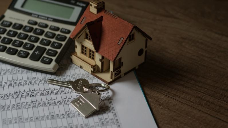 Imagem de uma miniatura de casa em cima de folha de papel com vários números e ao lado de uma calculadora - Metrópoles