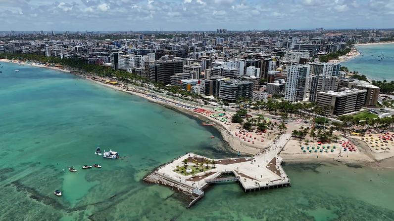 Vista aérea da orla de Maceió, em dia ensolarado, com mar azul e prédios na Ponta Verde/Jatiúca
