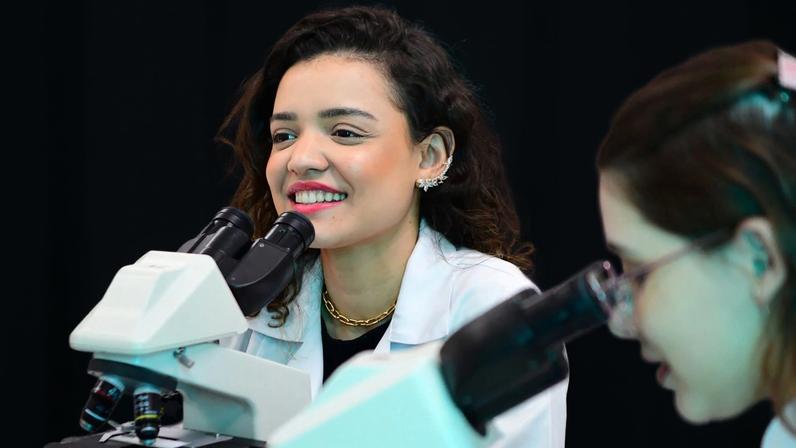 Profissionais em laboratório biomédico, com jalecos e microscópios, em ambiente moderno e iluminado