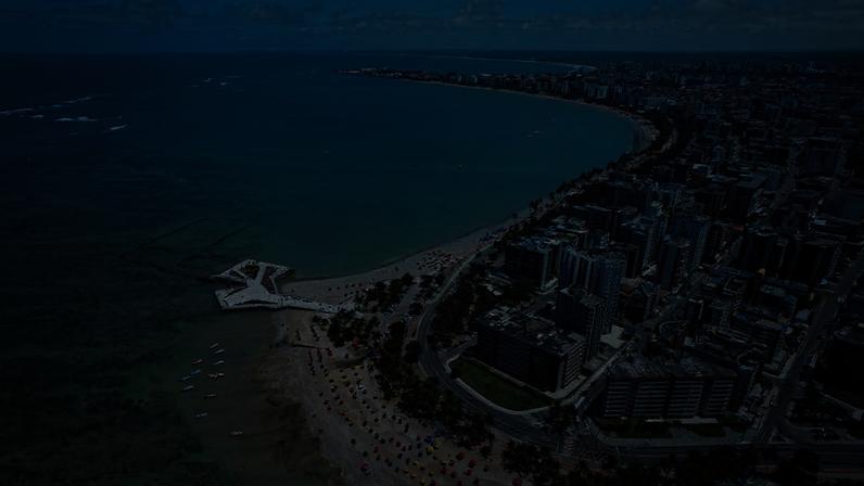 Vista aérea da orla de Maceió com mar verde-azulado, edifícios e coqueiros.
