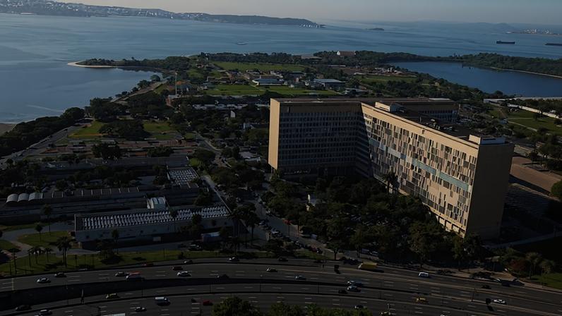 Vista aérea da Cidade Universitária da UFRJ na Ilha do Fundão, com edifícios, áreas verdes e água ao fundo
