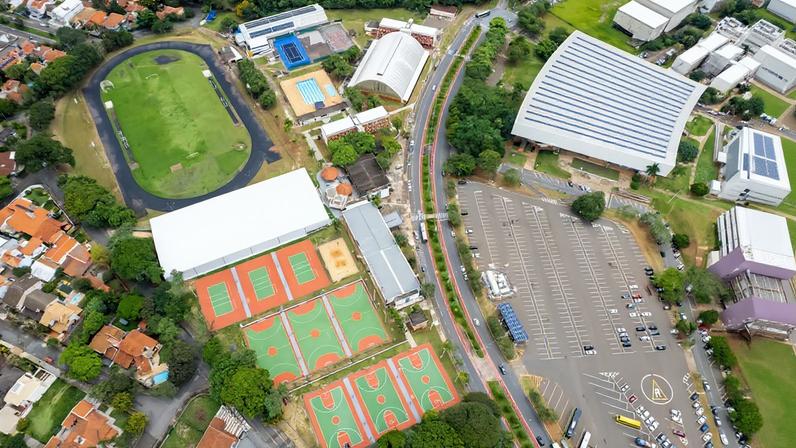 Vista aérea do campus em Campinas, com áreas esportivas, prédios acadêmicos e arborização.