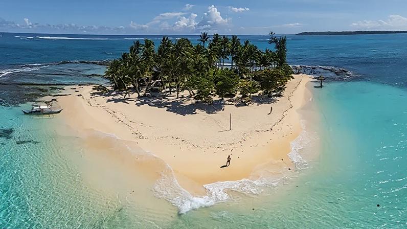 Getty Images Aerial view of a tiny tropical sand island surrounded by shallow turquoise water and lined with palm trees (Credit: Getty Images)