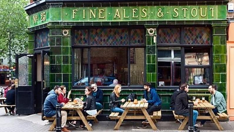 Alamy People sit outside a green-tiled pub in London on wooden benches with gold lettering reading 'Fine Ales and Stout' (Credit: Alamy)