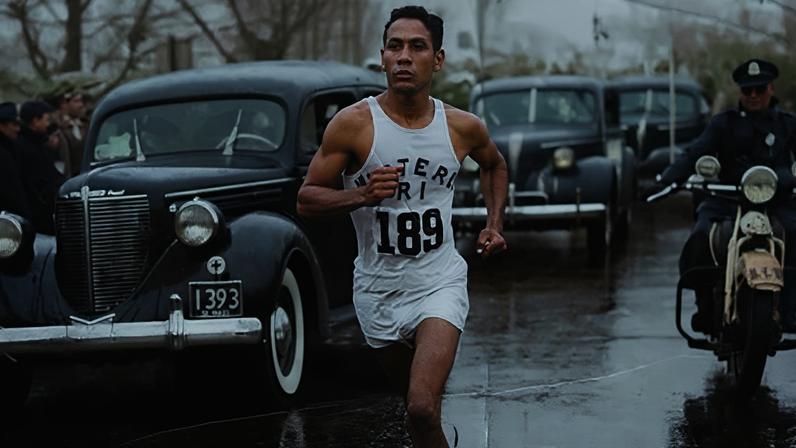 Sepia photograph of Ellison "Tarzan" Brown running down a Boston street with cars and a motorcycle trailing behind him