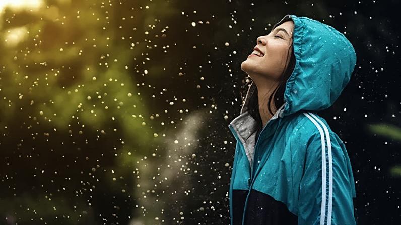 Getty Images A woman in a green sports jacket with the hood up smiles as she leans her head up, eyes closed, towards the falling rain (Credit: Getty Images)
