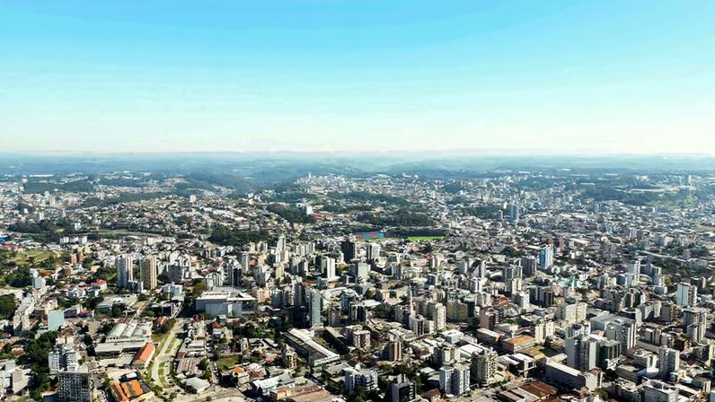 Vista aérea de uma praça central com igreja matriz e rua arborizada, céu azul.