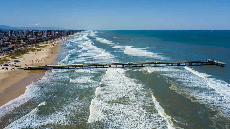 Praia urbana no Litoral Norte do RS, com píer sobre as ondas