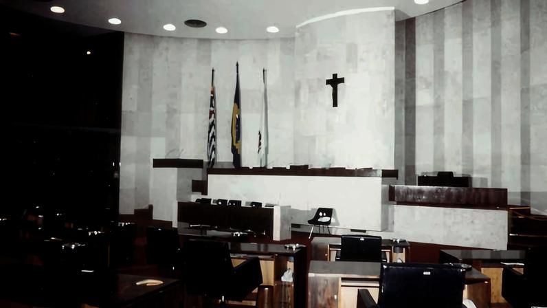 Plenário de uma câmara municipal, com cadeiras e microfones, em ambiente iluminado