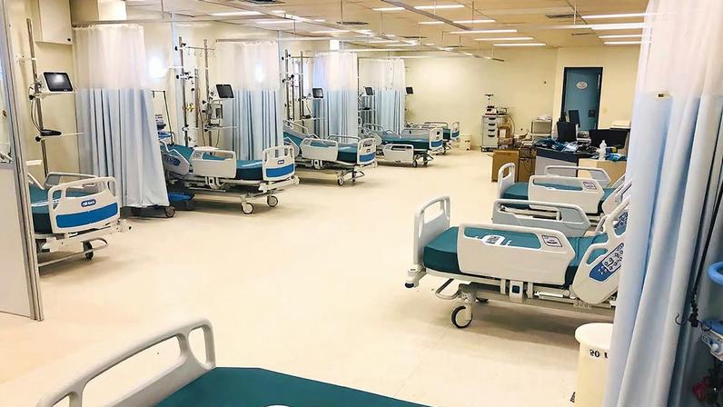 Corredor de hospital com várias camas e cortinas; ambiente profissional e organizado.