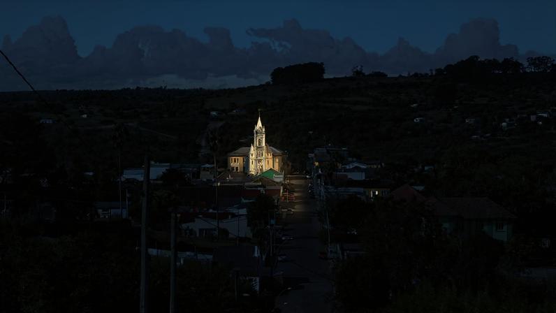 Vista aérea de pequena cidade do interior do Rio Grande do Sul, com igreja central e área urbana rodeada por lavouras ao entardecer
