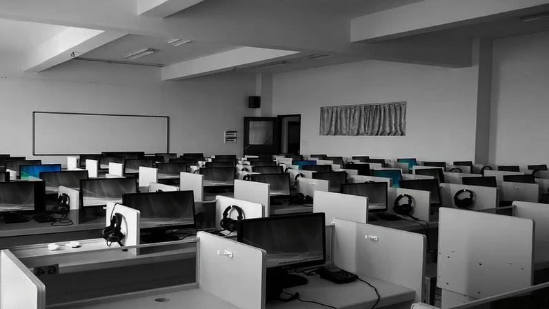 Laboratório de informática universitário moderno, com mesas em fileiras e estudantes programando em computadores de mesa