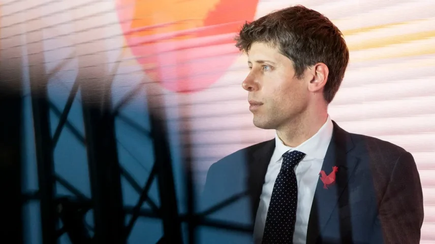 Sam Altman, CEO da OpenAI, de perfil com terno escuro, camisa branca e gravata preta com bolinhas brancas, broche de galo vermelho. Fundo listrado em laranja, amarelo e branco, com círculo laranja, e silhueta de estrutura metálica à frente.