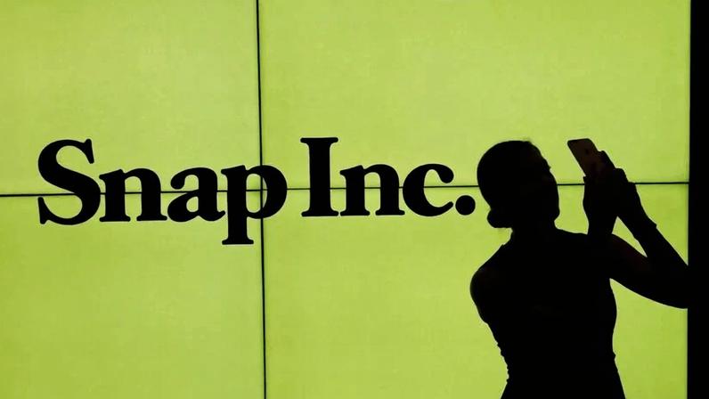 Uma mulher fica em frente ao logotipo da Snap Inc. no pregão da Bolsa de Valores de Nova York enquanto espera a Snap Inc. publicar sua IPO