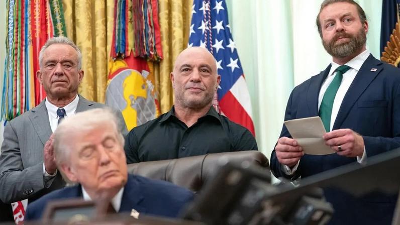 Trump na assinatura da ordem executiva neste sábado (18), com o secretário de Saúde, Robert F. Kennedy Jr., e o podcaster Joe Rogan (de camisa preta) ao fundo (Foto: ALLISON ROBBERT/EFE/EPA)
