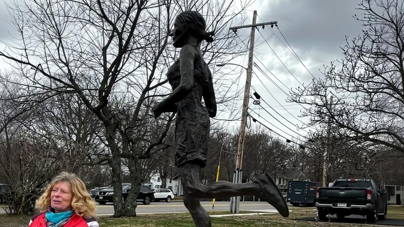 Bobbi Gibb stands in front of her bronze self-portrait at a ribbon cutting ceremony for the statue, March 27, 2026, in Hopkinton, Mass. (AP Photo/Jimmy Golen)