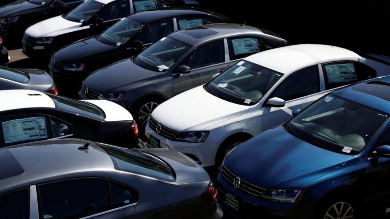 Vista aérea de pátio de concessionária com carros Volkswagen sedans novos, de cores variadas, estacionados.