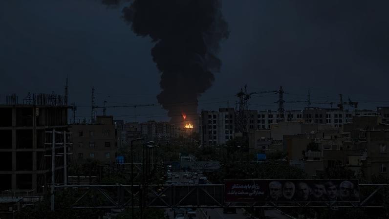 Portraits of Iranian military generals and nuclear scientists, killed in Israel's June 13 attack are displayed above a road, as a plume of heavy smoke and fire rise over an oil refinery in southern Tehran, after it was hit in an overnight Israeli strike, on June 15, 2025. Iran fired a fresh barrage of missiles at Israel, state television announced early on June 15, as the rivals exchanged fire for a third day. (Photo by ATTA KENARE / AFP) (ATTA KENARE/AFP)