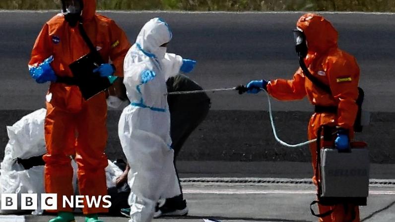 passenger in white is screened by health workers in orange in tenerife