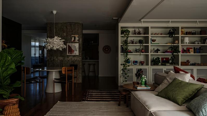 LIVING INTEGRADO | No espaçoso living, alguns itens foram reaproveitados, como o piso original de tábua corrida de madeira ipê e a estante existente, projetada pela arquiteta para os pais e agora modernizada com pintura em laca. Nela, estão objetos de acervo da família mesclados com cerâmicas de Beth Rocha, peças do Studio Grabowsky, quadros do Olli Atelier, recordações de viagens e plantas, entre elas jiboia, imbé-furado, planta-cesta e rabo-de-burro, que fazem parte do projeto paisagístico de Anna Luiza Rothier. Para o vaso no viso, ela escolheu 'Anthurium plowmanii'.Tapetes da Galeria Hathi. No pilar de concreto, revelado durante a obra, quadros do Studio Grabowsky e Casa Ocre