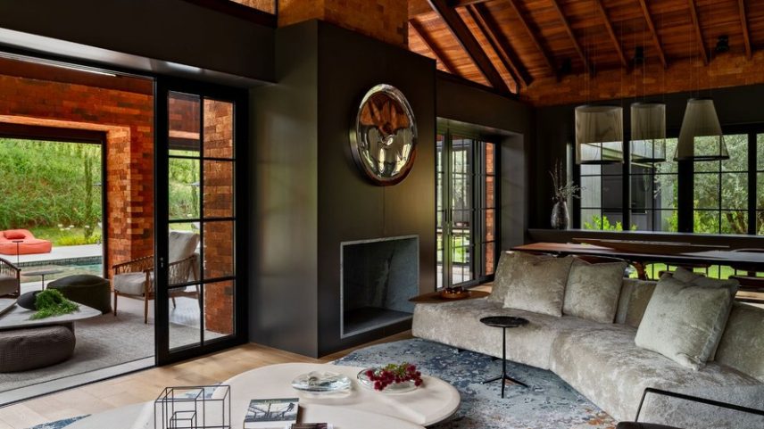 LIVING | A estrutura da casa em tijolinhos ganhou detalhes escuros, como os painéis de parede sob medida de laca cinza, realizados pela JCS Marcenaria, onde se destaca a escultura em inox Epicentro, de Jacqueline Terpins, sobre a lareira de pedra-sabão, da Paglioto. Entre o mobiliário, peças de design assinado, como o sofá Landscape, de Fernanda Marques para Breton; mesas de centro Blast, de Ronald Sasson, na Micasa; e mesa de apoio Jazz, de Jader Almeida. Sobre o piso de assoalho em carvalho europeu customizado Nature Brown, da Parket, está o tapete sob medida da Botteh