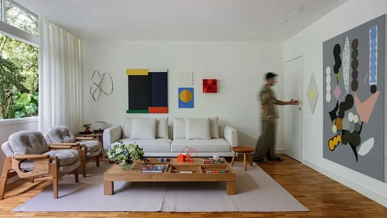 SALA DE ESTAR | As paredes brancas destacam as obras de arte, como a maior da direita, de Paulo Whitaker, ao lado do quadro menor, de Hércules Barsotti. O piso de taco de peroba-do-campo foi restaurado para trazer calor e autenticidade ao projeto, repleto de móveis de design brasileiro. Sofá da Way Design, par de poltronas Tetê, de Sergio Rodrigues, na mesma loja, e banco Mocho, do mesmo autor, na Arquivo Contemporâneo, loja que também forneceu a mesa de centro Rosá, de Maria Cândida Machado. Sobre ela, destaca-se uma escultura de José Bechara. Tapete em algodão da Galeria Hathi. Cortina de linho da Cortinaria