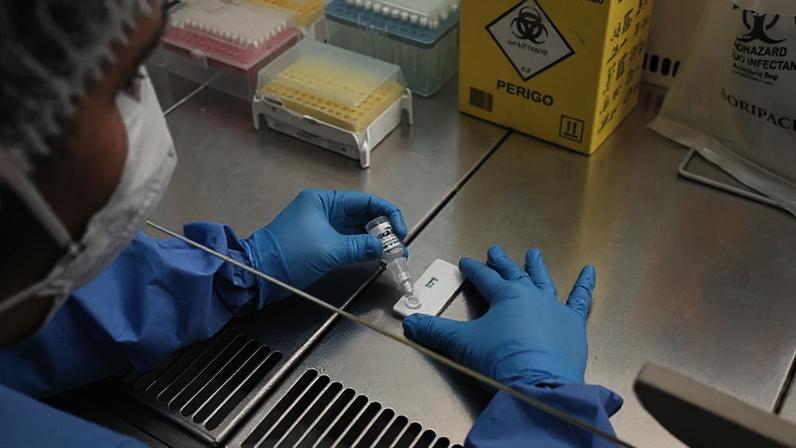 Mulher de luvas e usando equipamentos de proteção faz teste em um laboratório