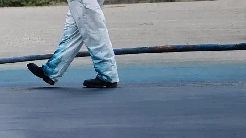 A photo of a construction crew member walking across the bottom of the Reflecting Pool as blue paint is being applied.
