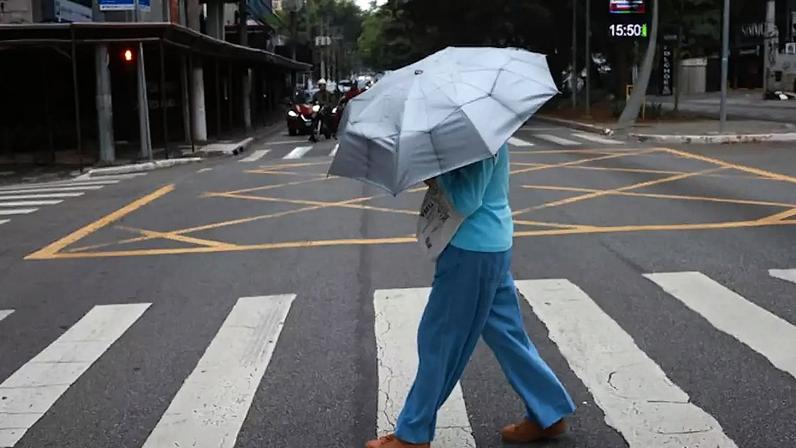 Na foto, pedestre se protege de chuva fina e baixa temperatura.