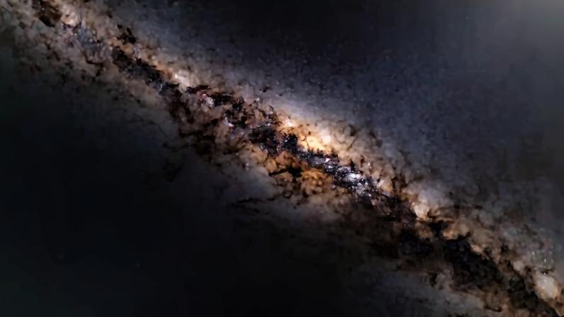 Via Láctea com bilhões de estrelas brilhantes, nuvens de gás e poeira em tons de marrom, laranja e roxo, atravessando um céu noturno escuro