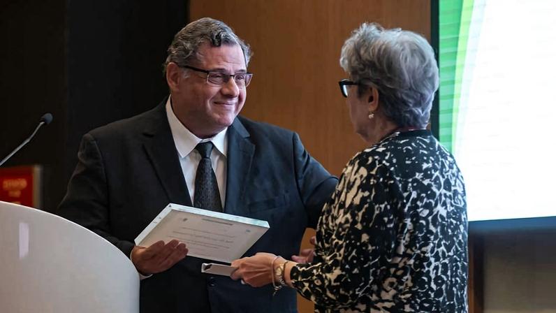 O professor Roger Chammas entrega a placa à Valeria Buccheri, mulher do professor José Eluf Neto, durante homenagem póstuma no Prêmio Octavio Frias de Oliveira, realizado no auditório do Icesp, em São Paulo