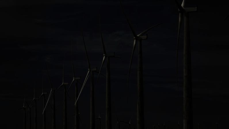 Linha de turbinas eólicas alinhadas em terreno plano sob céu azul com poucas nuvens. As hélices estão em diferentes posições, indicando movimento.