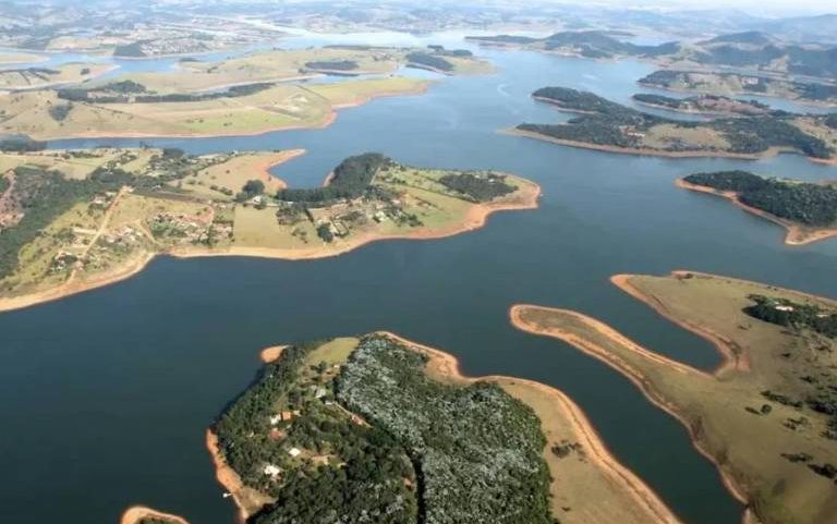 Reservatório de água com várias ilhas e penínsulas de terra cercadas por água. Vegetação verde cobre as áreas terrestres, e o céu claro é visível ao fundo.