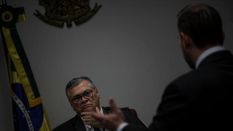Ministro do Supremo Tribunal Federal sentado, com expressão atenta, observa colega que fala em sessão. Bandeira do Brasil e brasão da República ao fundo.