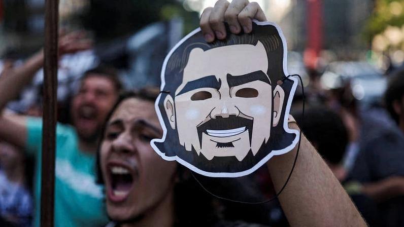 Manifestante em protesto contra corrupção segura máscara com ilustração de Daniel Vorcaro após escândalo do Master