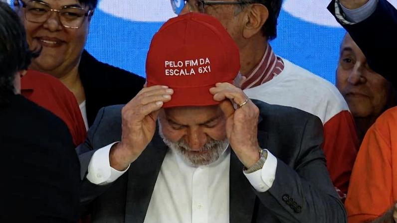 O presidente Lula, durante reunião com centrais sindicais no Palácio do Planalto, coloca sobre a cabeça um boné vermelho com a frase "PELO FIM DA ESCALA 6X1".