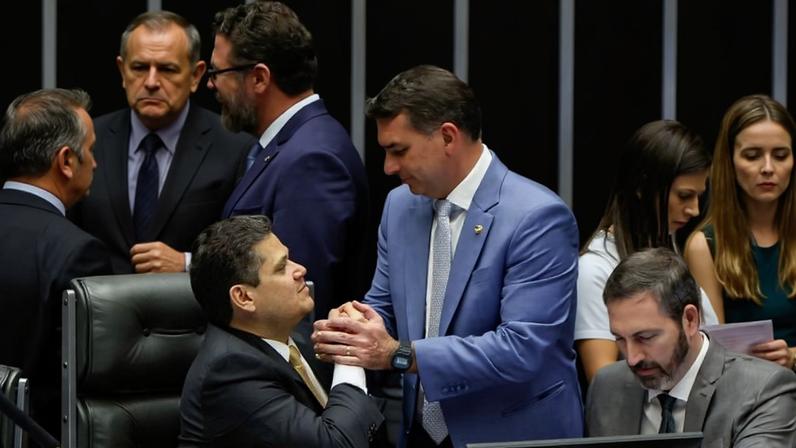 O senador Flávio Bolsonaro (PL-RJ) cumprimenta o presidente do Senado, Davi Alcolumbre (União-AP), durante a sessão do Congresso Nacional que derrubou o veto ao projeto da dosimetria.