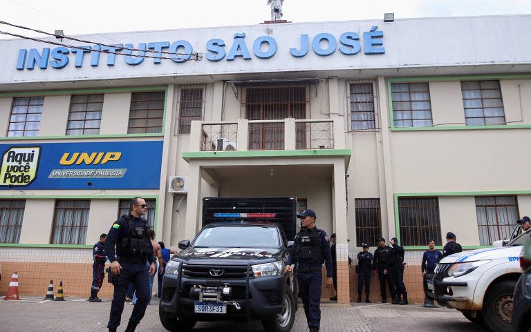 Vários policiais em frente ao Instituto São José, com viaturas estacionadas na entrada principal do prédio. Fachada do instituto com letreiro azul e placa da UNIP ao lado.
