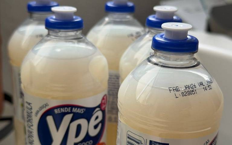 Seis garrafas transparentes de detergente líquido Ypê Coco com tampa azul, alinhadas em superfície branca. O líquido é de cor creme clara e as etiquetas exibem o nome da marca e informações do produto.
