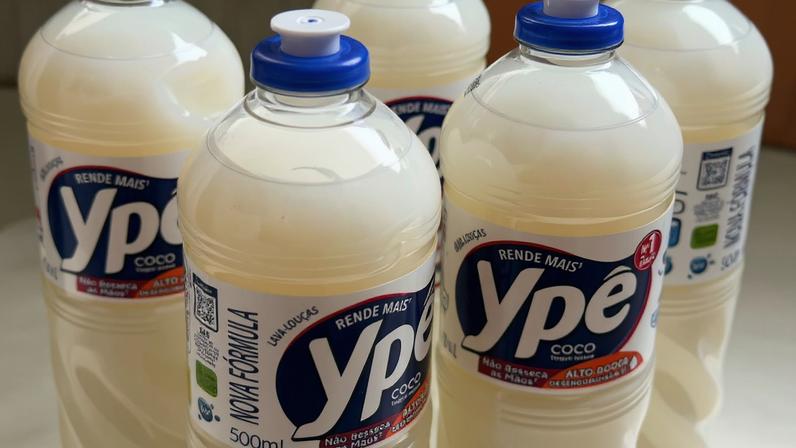 Cinco garrafas transparentes de detergente líquido Ypê coco, com tampa azul, dispostas em superfície clara. Rótulos exibem marca, volume de 500 ml e informações de fabricação.