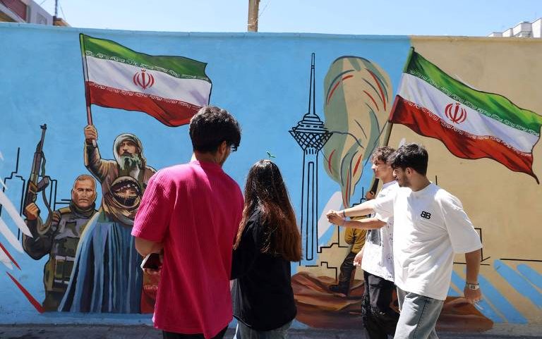 Iranianos caminham ao lado de um mural anti-EUA e anti-Israel pintado em uma parede na capital Teerã